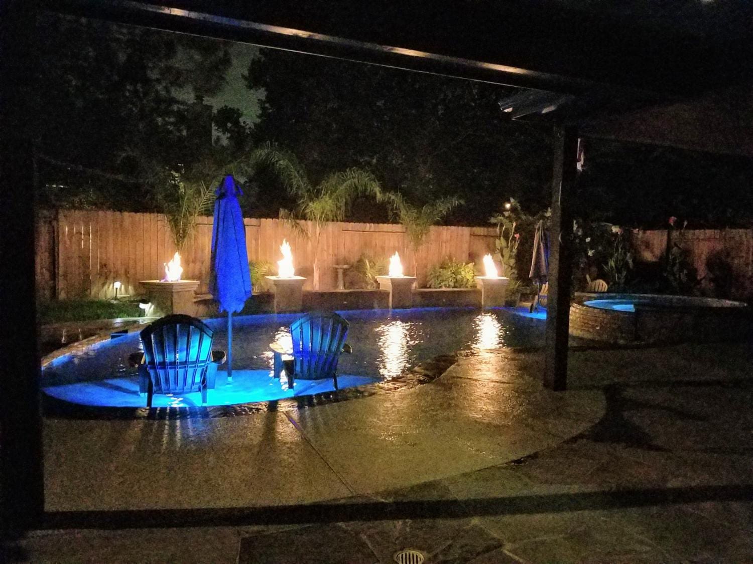 A patio with chairs and an umbrella lit up at night.